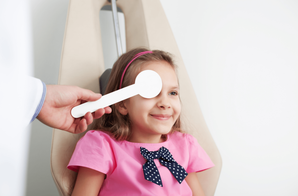 A young girl sitting in a chair at the optometrist's office while she performs a vision test with the optometrist