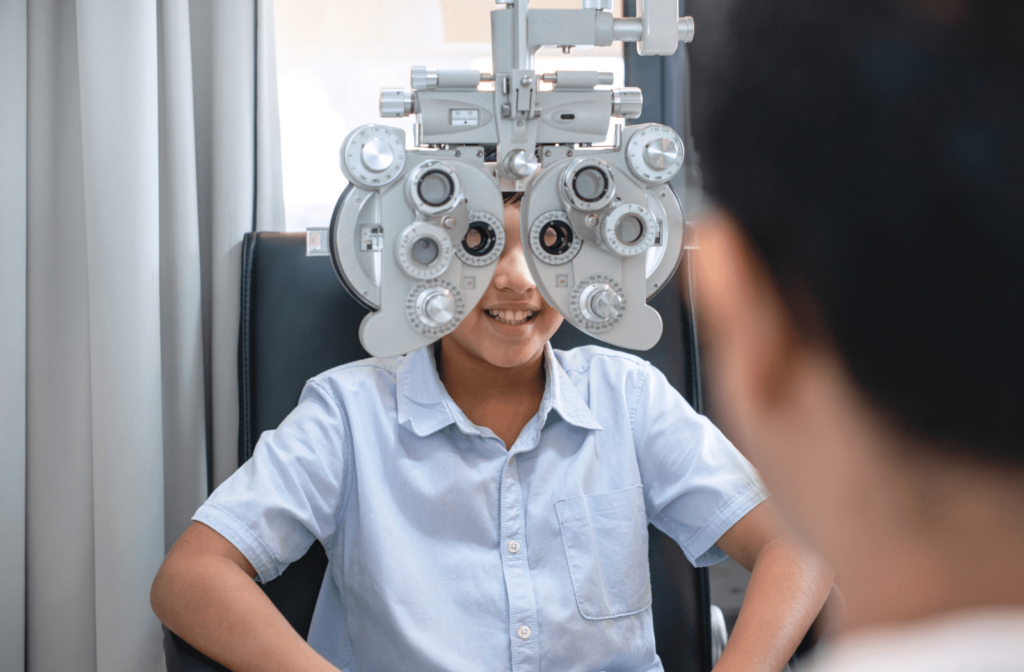 A young boy sitting behind a phoropter at the optometrists office