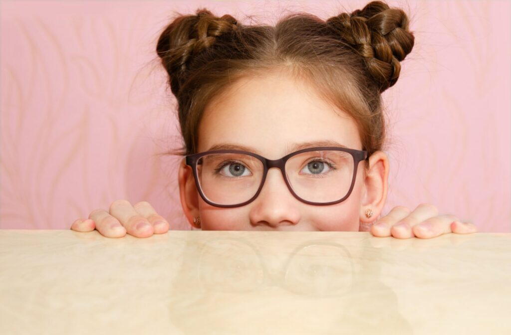 A young girl wearing glasses and peeking over a counter top